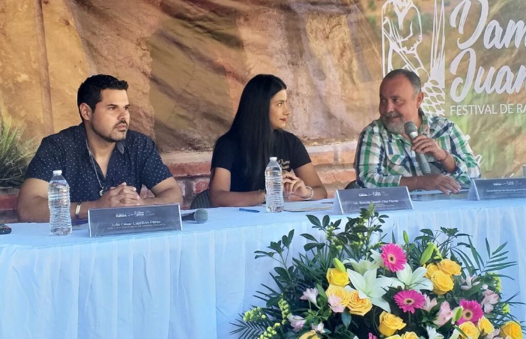 Tres personas en una mesa de presidium para presentar el festival DamaJuana.
