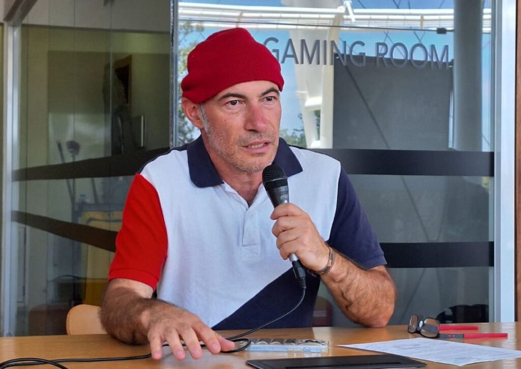 Hombre con gorra color roja hablando por micrófono. Antoniu V. Moldovan presenta su documental.