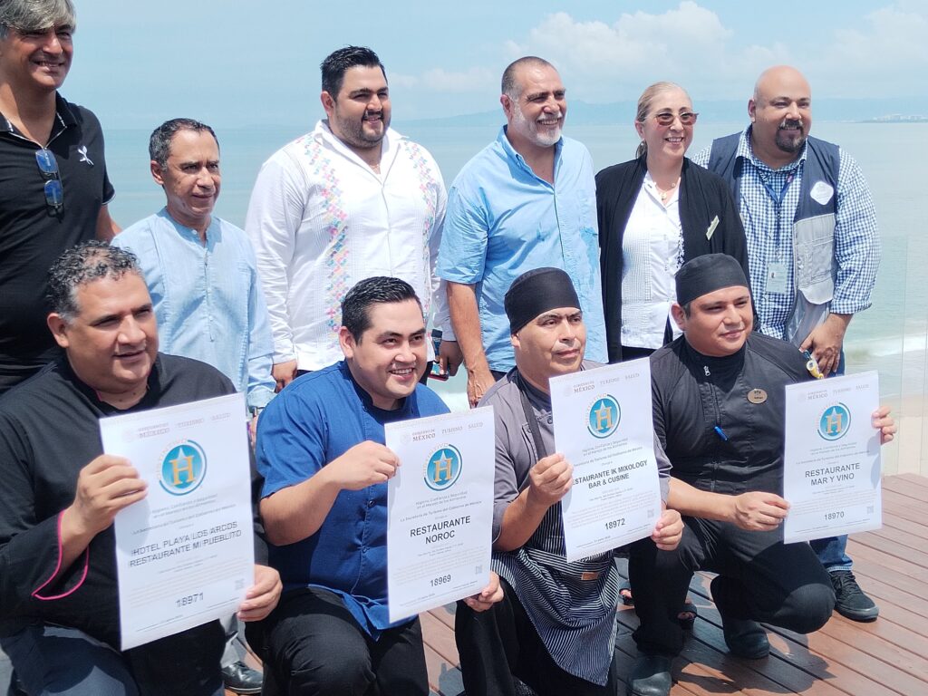 Un grupo de personas de espaldas a la playa sostienen Distintivos H.